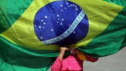 Eine brasilianisches Mädchen versteckt sich hinter der Brasilien-Flagge. © Imago/Agencia EFE