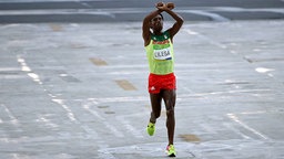Der Marathonläufer Feyisa Lilesa aus Äthiopien läuft mit gekreuzten Armen ins Ziel ein. © imago/Xinhua